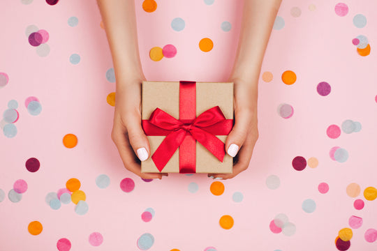 Woman,Hands,Holding,Present,Box,With,Red,Bow,On,Pastel