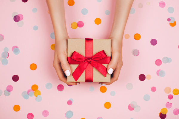 Woman,Hands,Holding,Present,Box,With,Red,Bow,On,Pastel