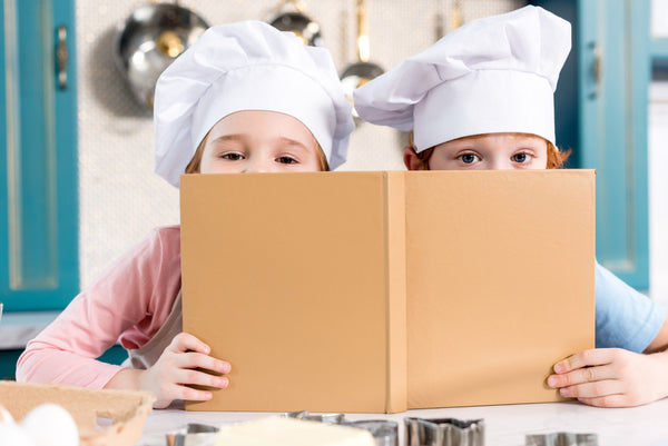 Cute,Children,In,Chef,Hats,Holding,Cookbook,And,Looking,At