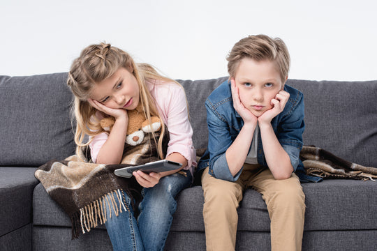Pre-adolescent,Bored,Brother,And,Sister,Sitting,On,Sofa,And,Holding